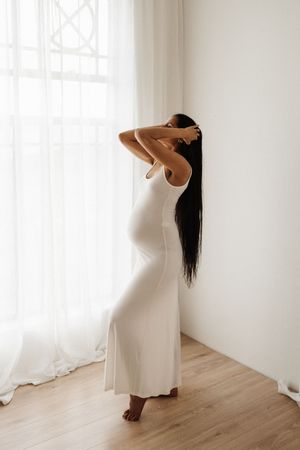 Pregnant woman in white dress stretches gracefully during maternity photoshoot.