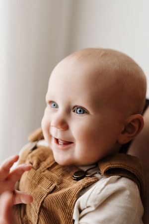 Happy baby wearing brown corduroy overalls smiles while looking to the side.