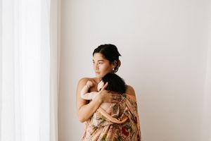 Intimate portrait of person wrapped in floral fabric standing beside window in soft natural light.