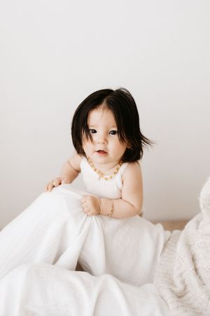 Portrait of small child in white dress sitting among soft blankets.