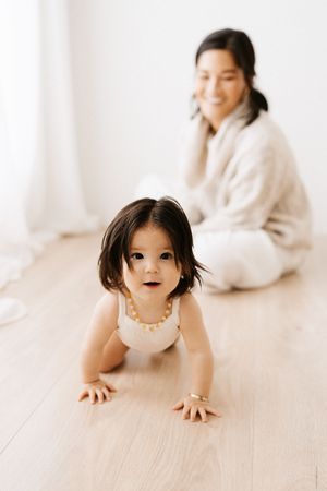 Indoor portrait of crawling toddler in white dress with natural window lighting.