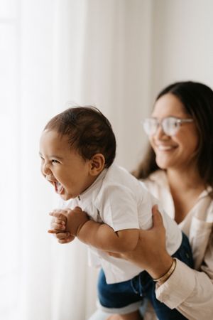 Joyful moment between parent and laughing baby against bright window.