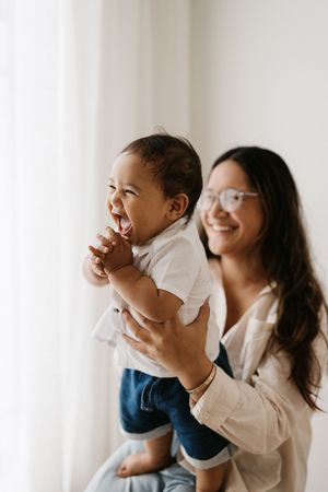 Parent lifting excited baby who shows pure joy against white curtain backdrop.