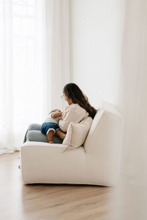 Side view of person sitting on white armchair in minimalist room with wooden floors.