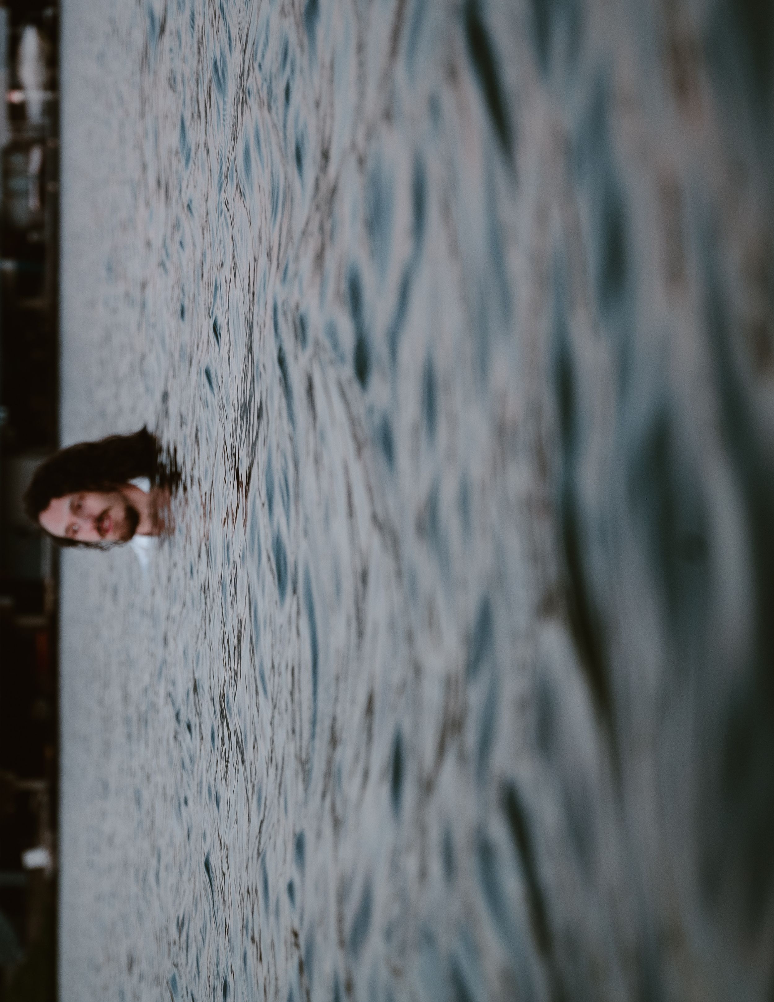 A figure emerges from rippling water creating an artistic reflection against the moody dark surface.