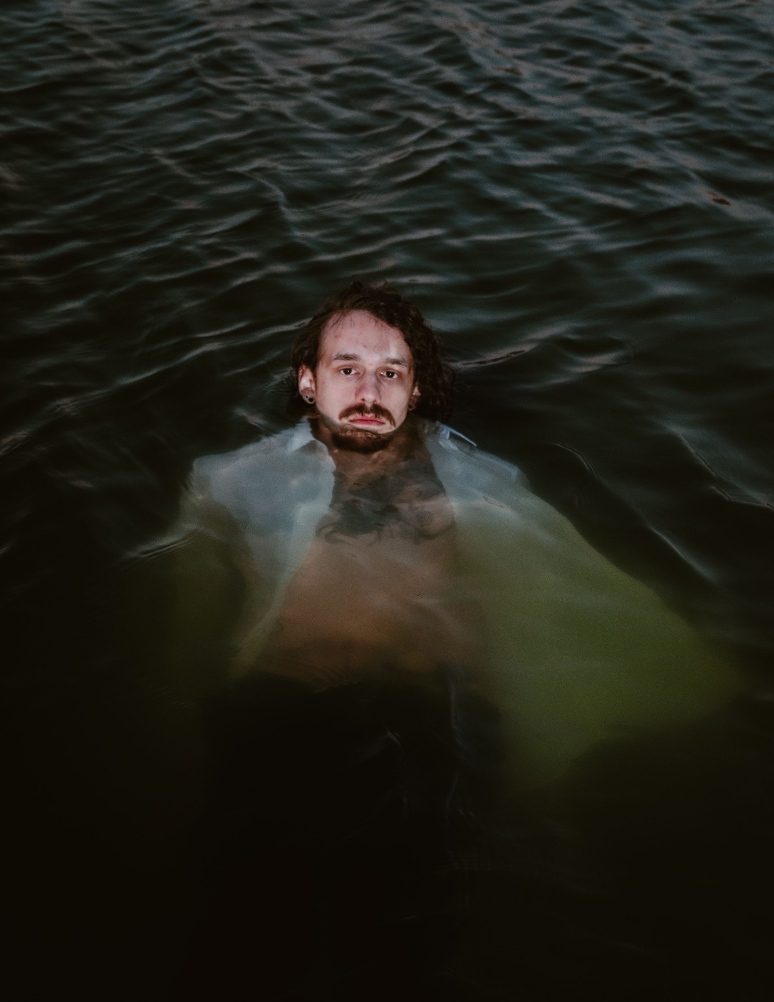 A figure emerging from dark waters with ripples surrounding them in moody atmospheric lighting.