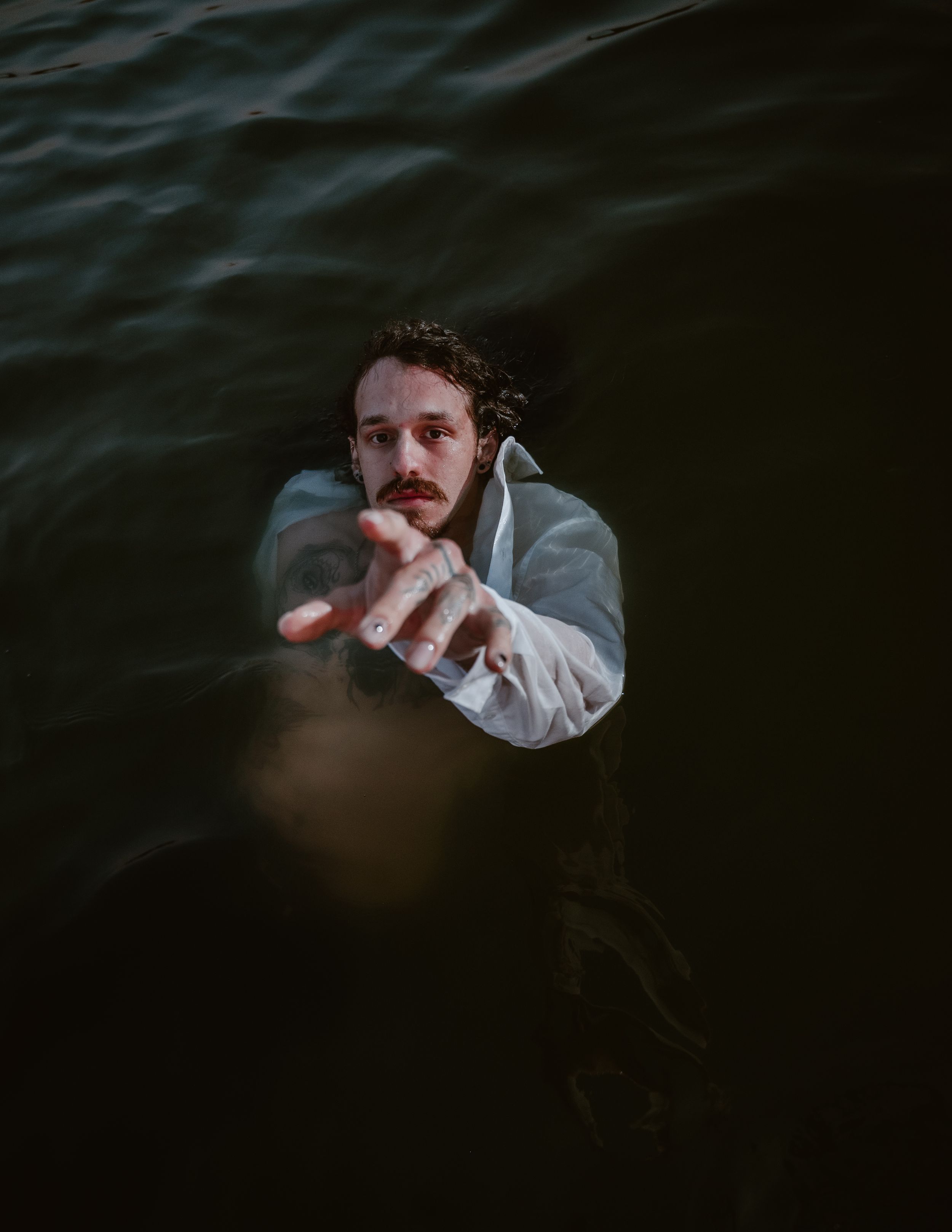 A figure in a white shirt emerges from dark moody waters in an artistic atmospheric portrait.