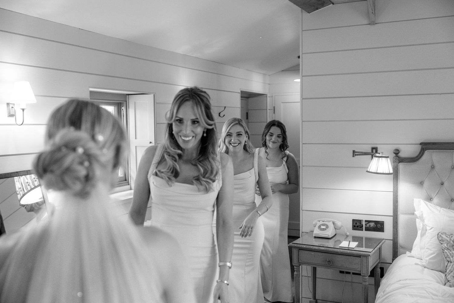Wedding preparation scene showing bride getting ready with bridesmaids in a rustic white wooden room.