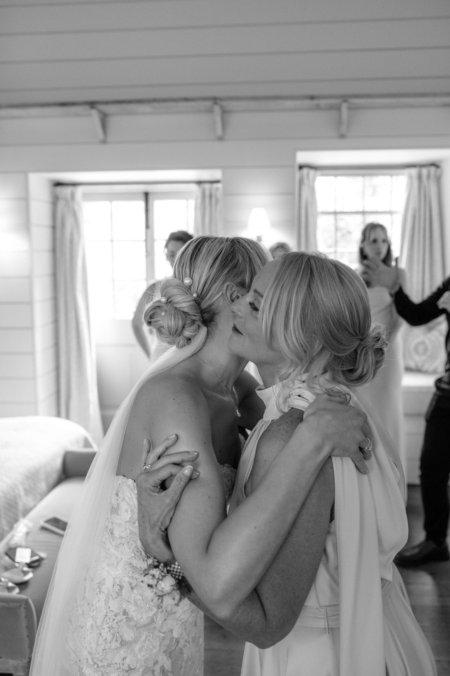 A tender moment between a bride and her loved one sharing a close embrace in a sunlit room.