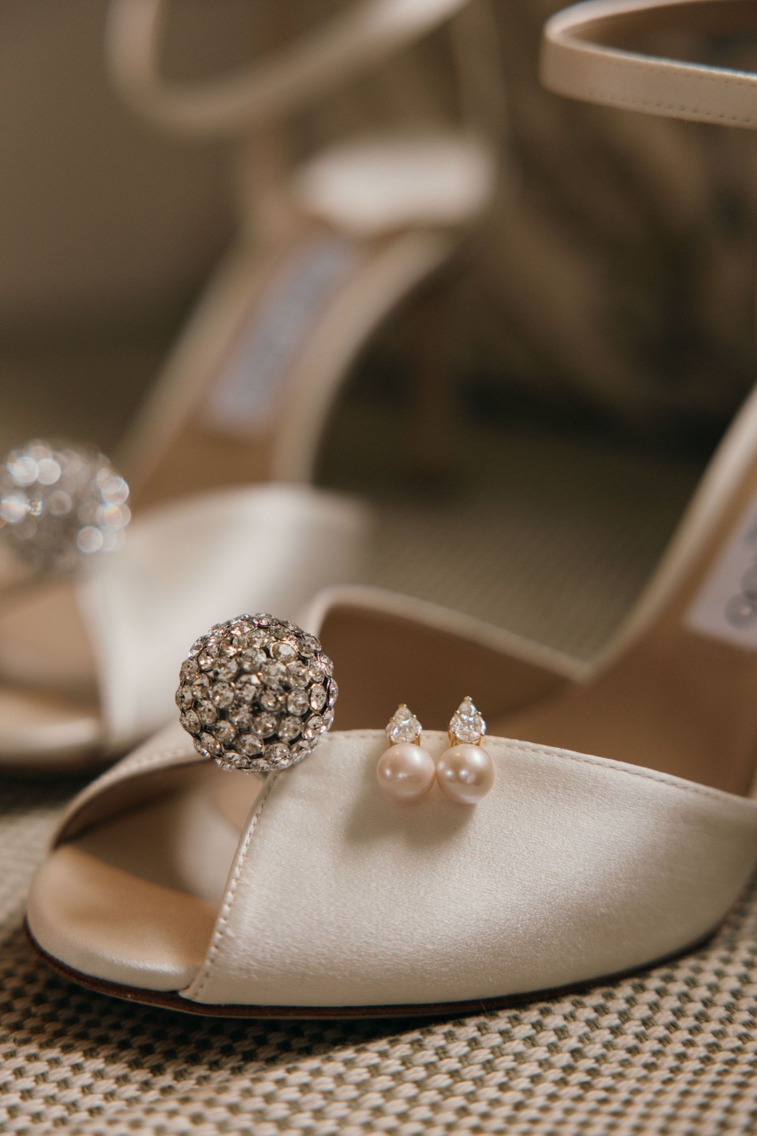 Elegant bridal accessories including a crystal brooch and pearl earrings resting on a white satin wedding shoe.