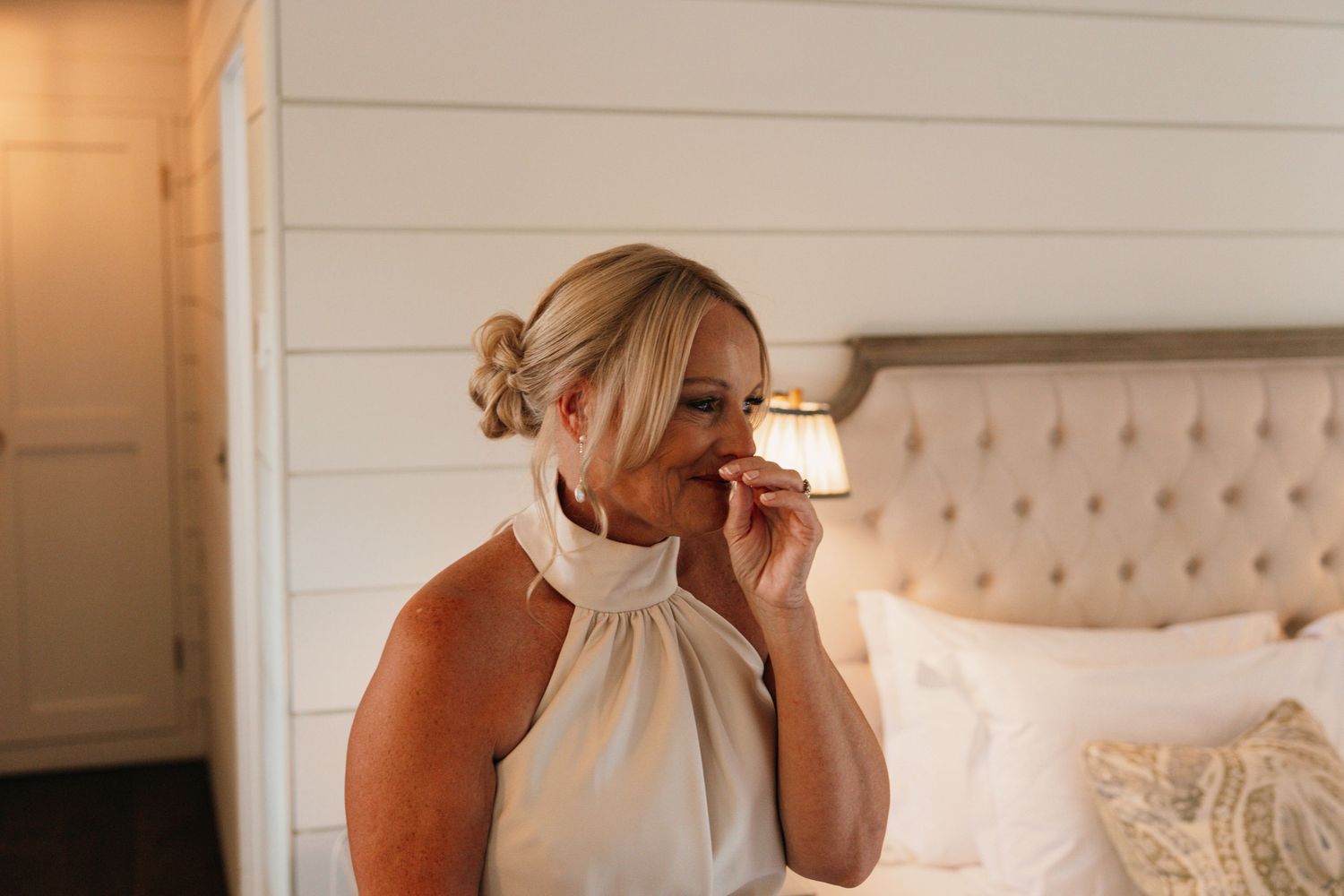 A person in an elegant white halter dress sits on a bed in a modern farmhouse-style bedroom.