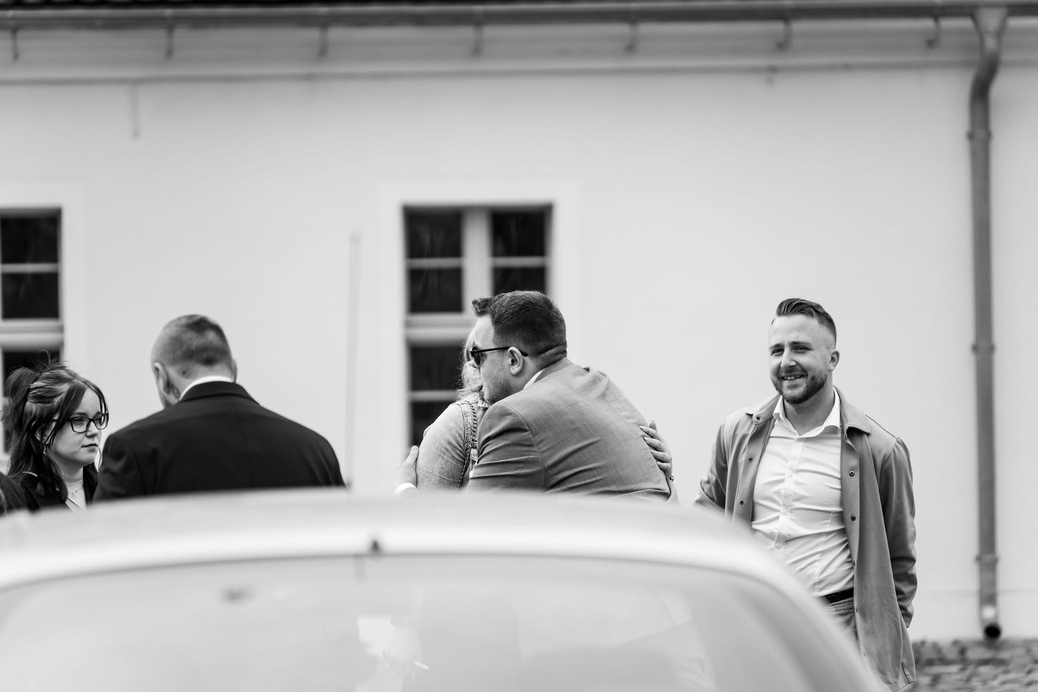 Bräutigam lacht mit Trauzeugen vor dem Auto, Schwarz-Weiß