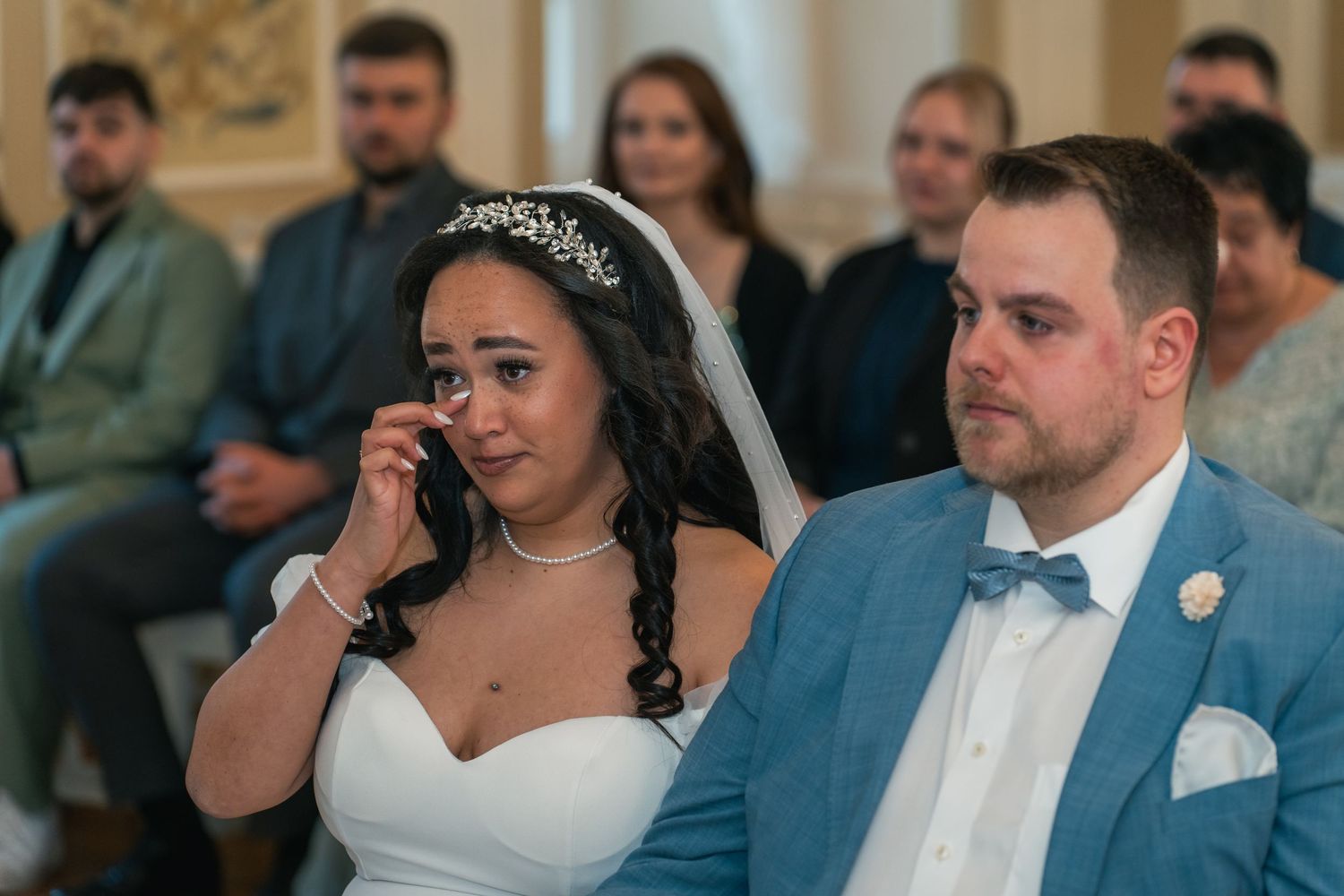 Braut mit Träne sitzt neben Bräutigam im Trausaal Schloss Vetschau, Gäste im Hintergrund