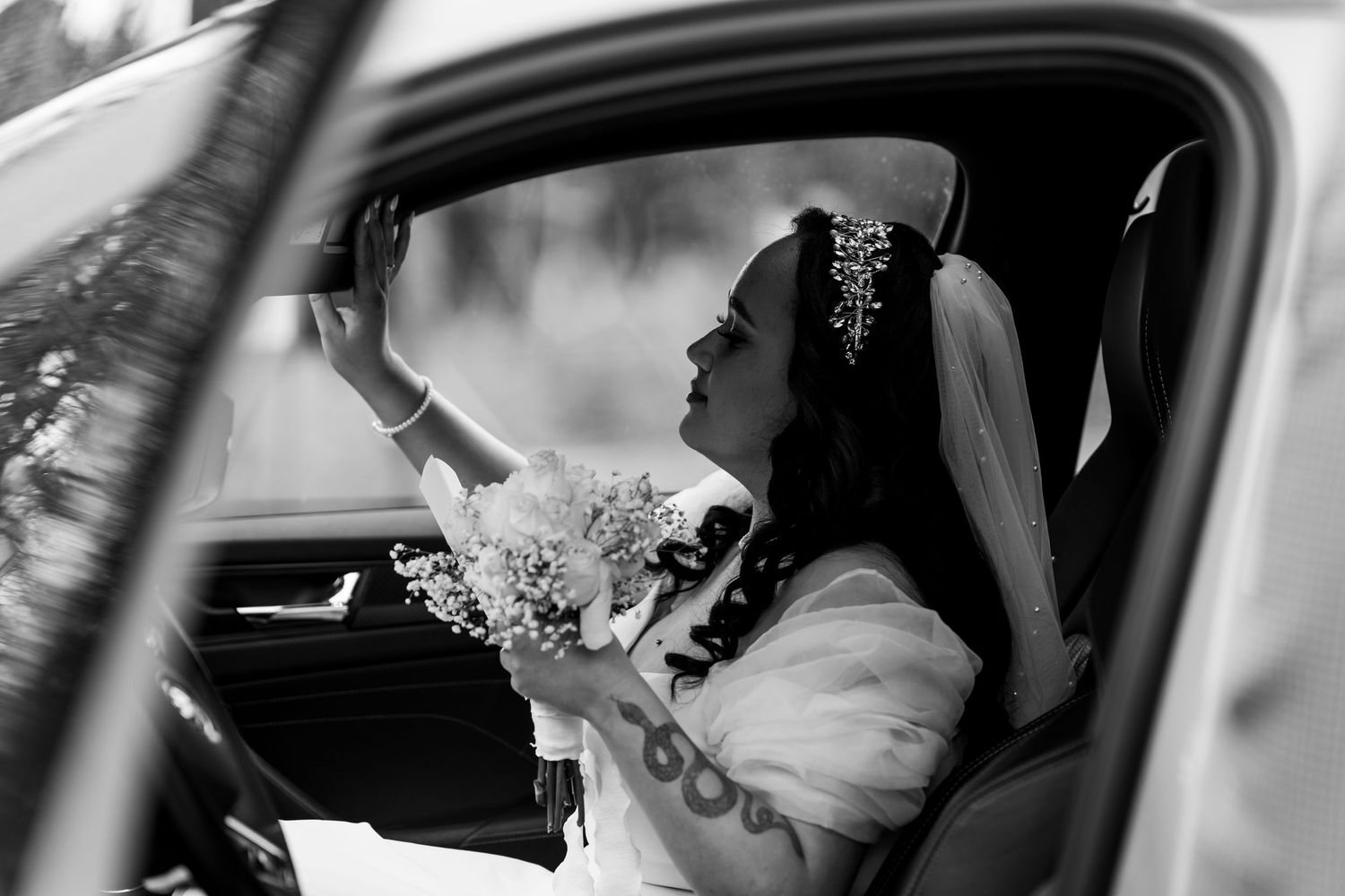 Braut sitzt mit Blumenstrauß im Auto, schaut aus dem Fenster