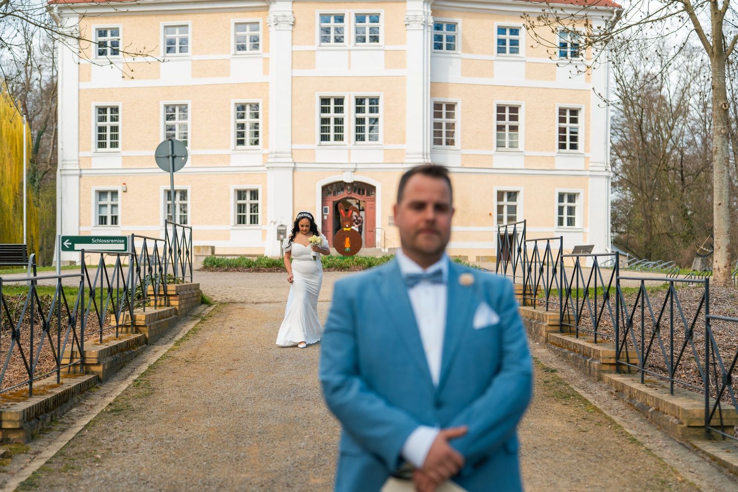 Bräutigam steht auf Brücke vor Schloss Vetschau, Braut im Hintergrund