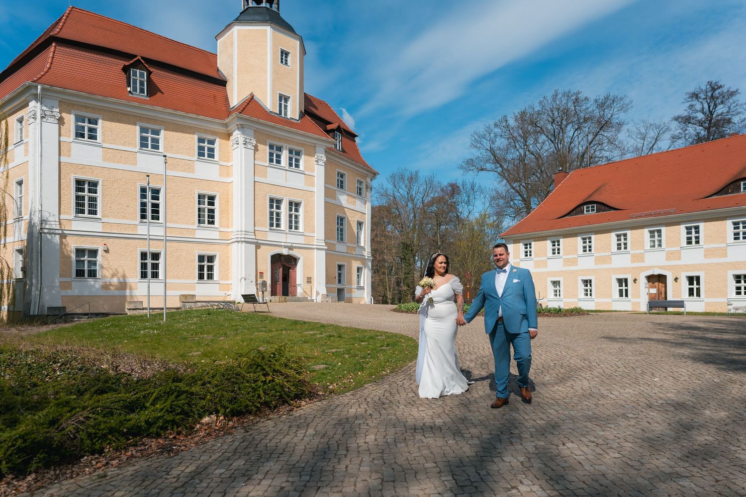 Brautpaar spaziert vor dem Schloss Vetschau, blauer Himmel