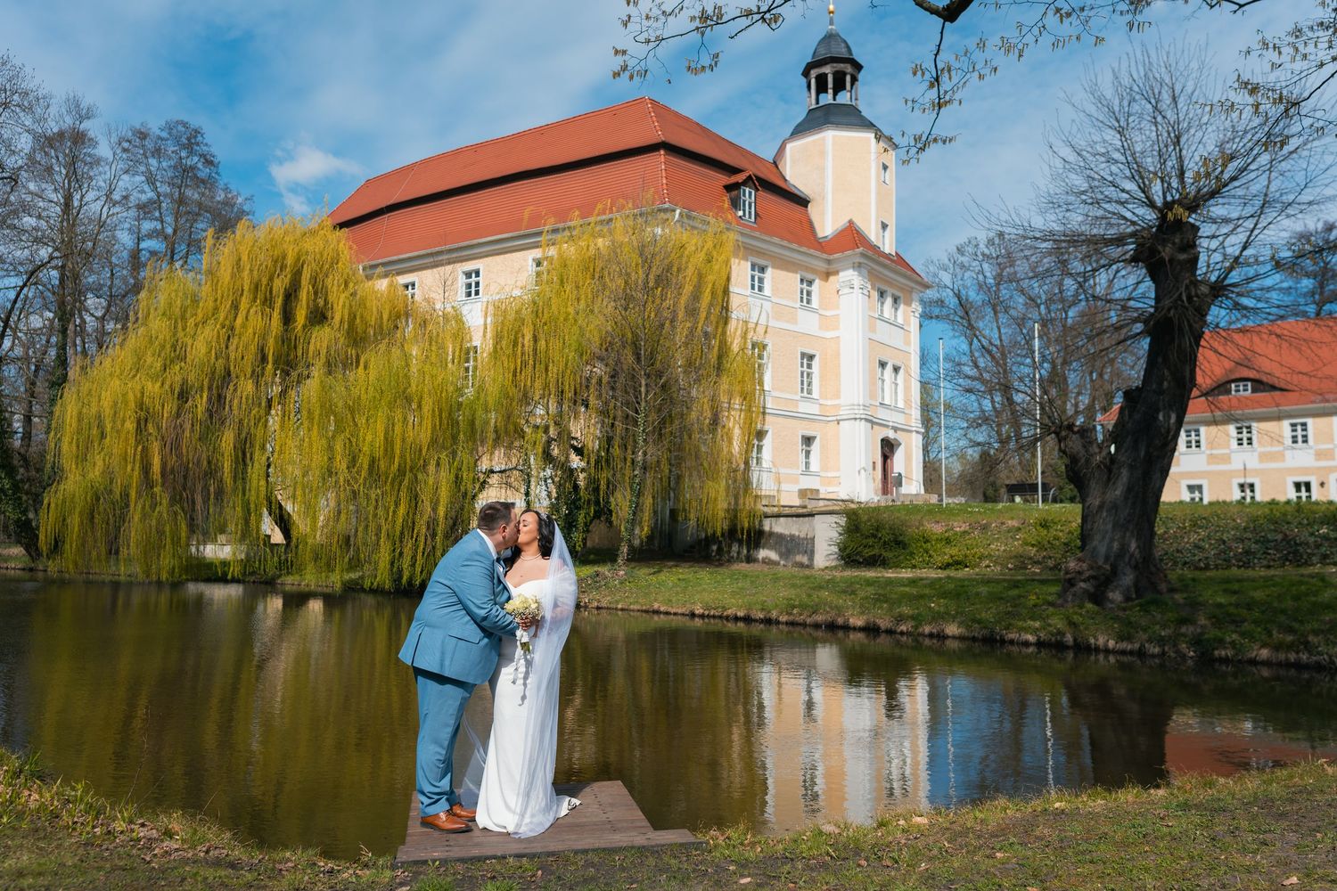 Brautpaar steht am Seeufer mit Schloss Vetschau im Hintergrund