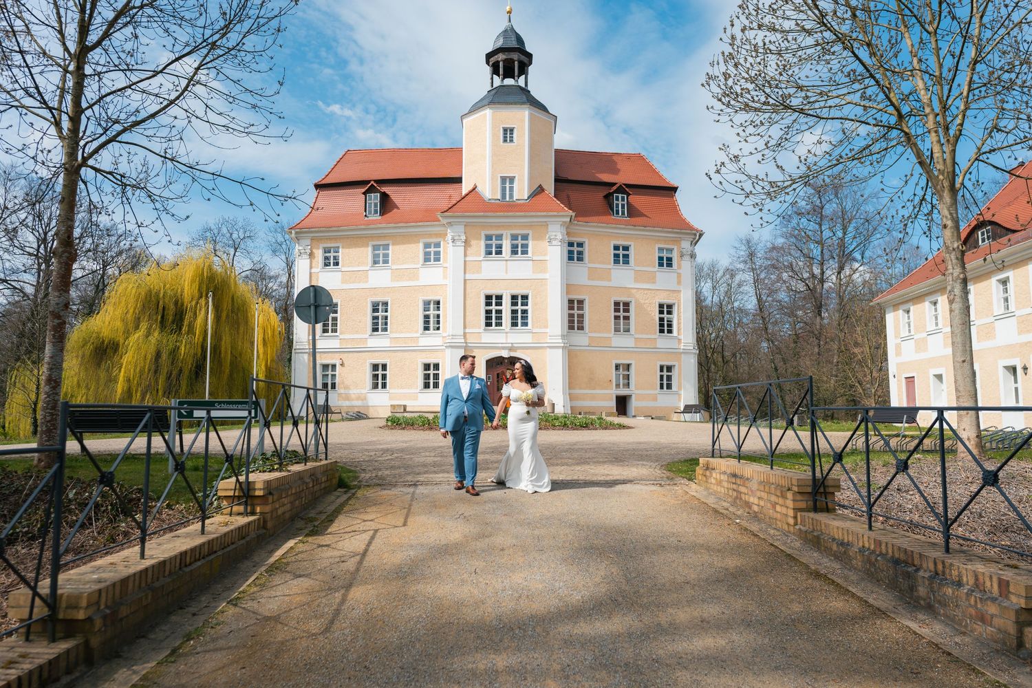 Brautpaar auf Brücke vor Schloss Vetschau, frontal mit blauem Himmel