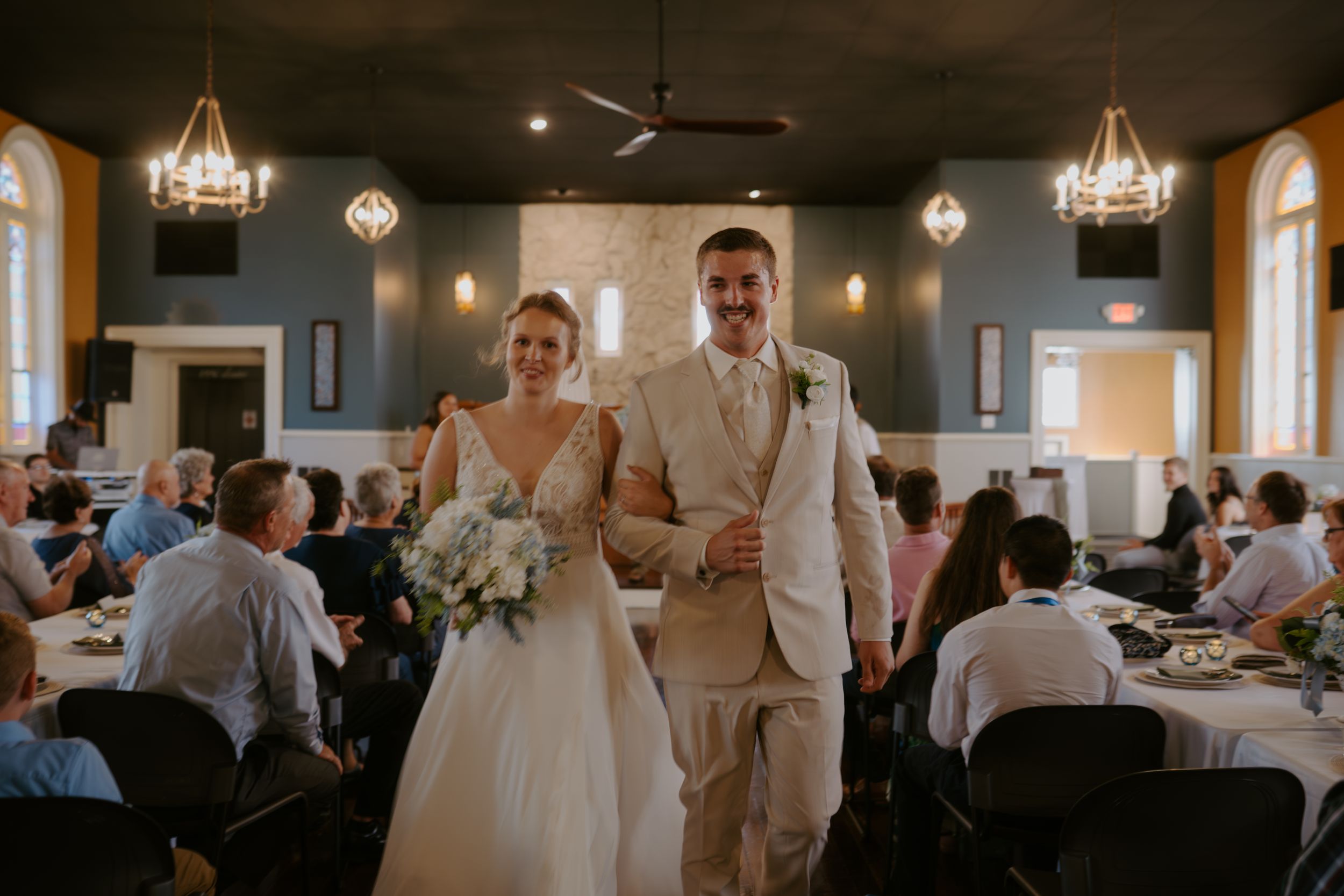 Wedding reception venue with elegant chandeliers and white tablecloths in a rustic indoor setting.
