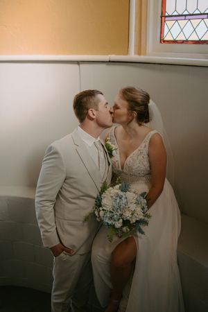 A romantic wedding moment captured in soft lighting against a neutral wall.