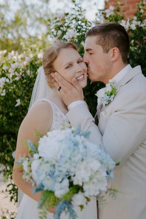 Romantic wedding portrait with light blue hydrangea bouquet against greenery.