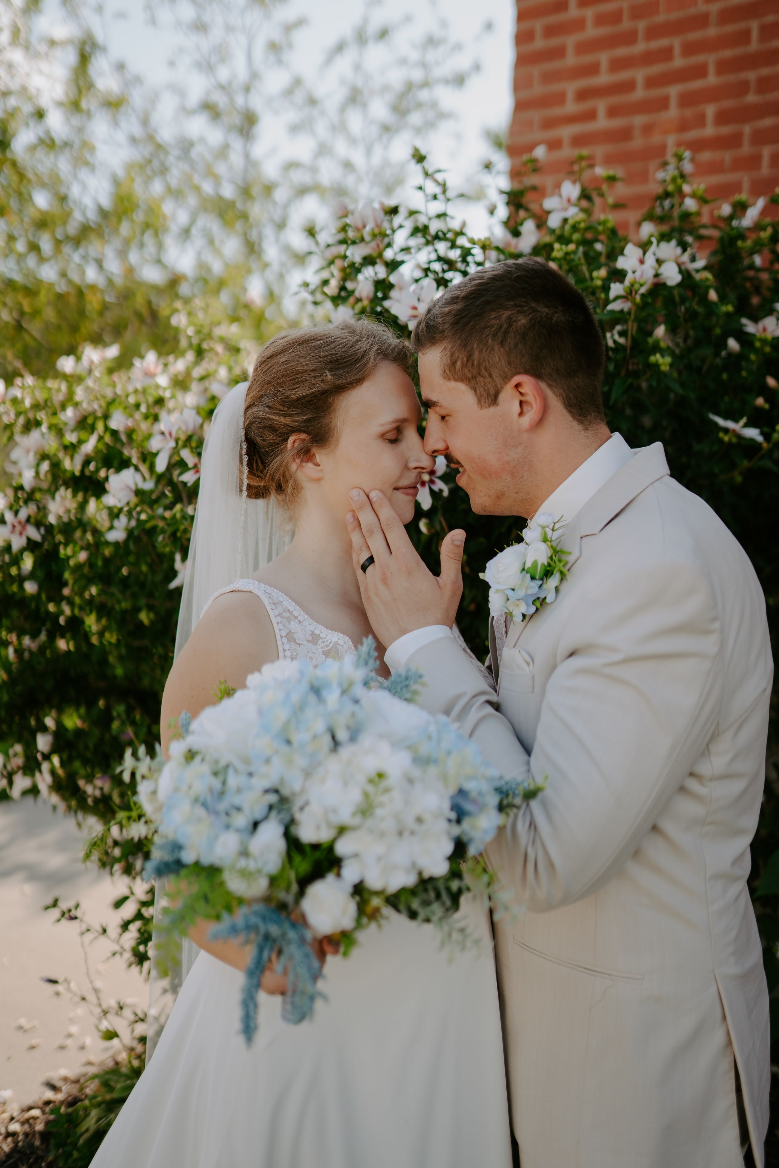 Romantic wedding portraits against red brick wall with blue and white bouquet.