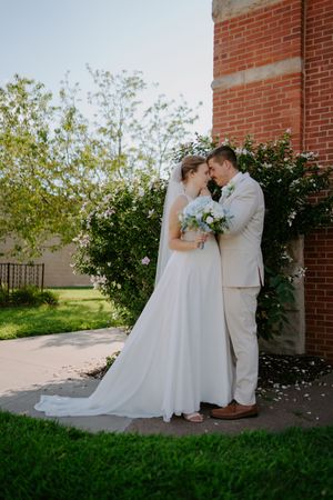 Intimate wedding portrait against brick architecture and garden landscaping.