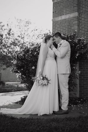 A romantic black and white wedding portrait by brick wall with flowing veil and bouquet.