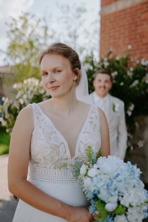 A person in a white lace wedding dress holds a blue and white hydrangea bouquet.