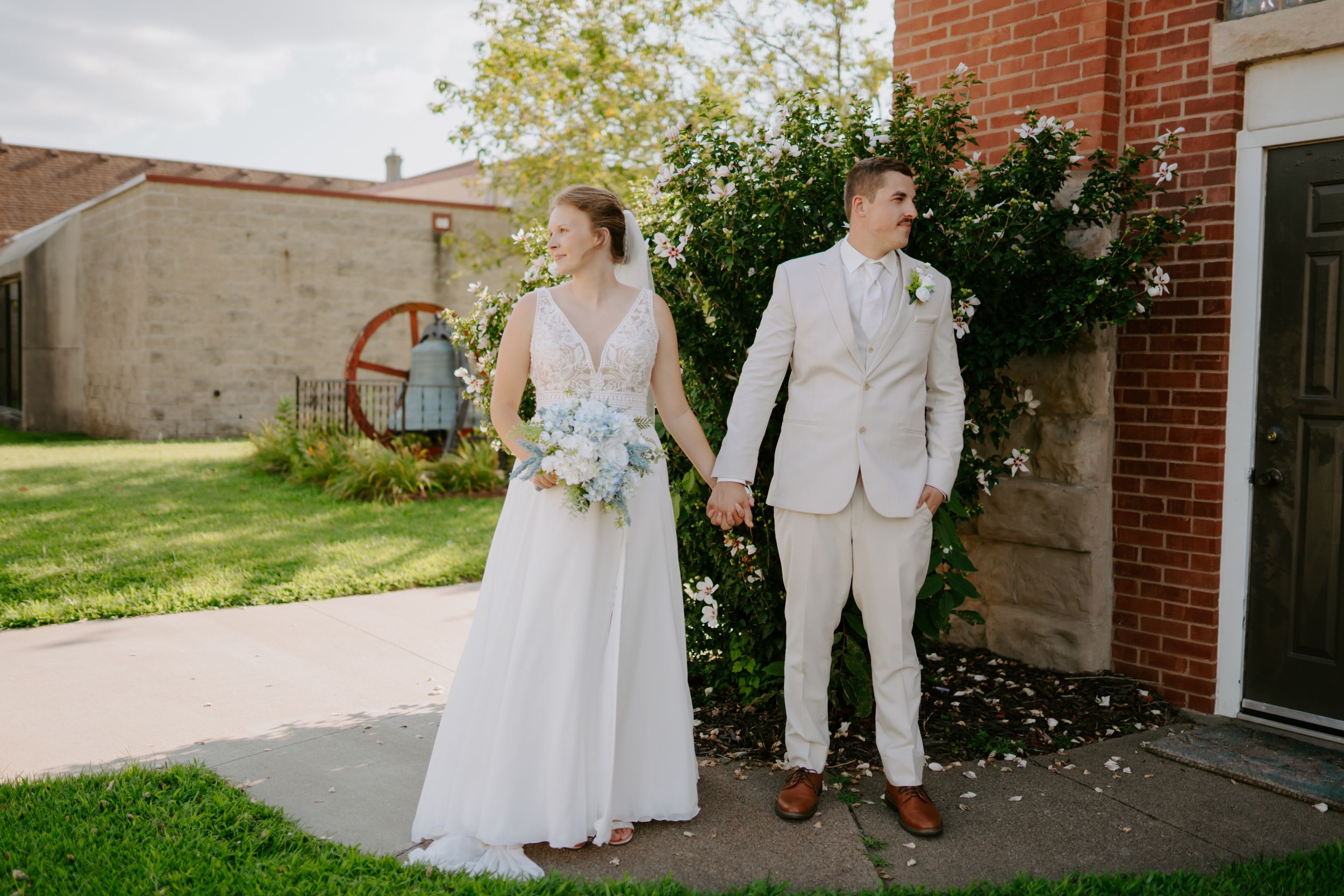 Wedding couple walking together outside brick building on sunny day.