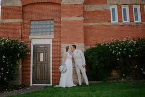 A wedding party poses for photos outside a historic brick building with white trim.
