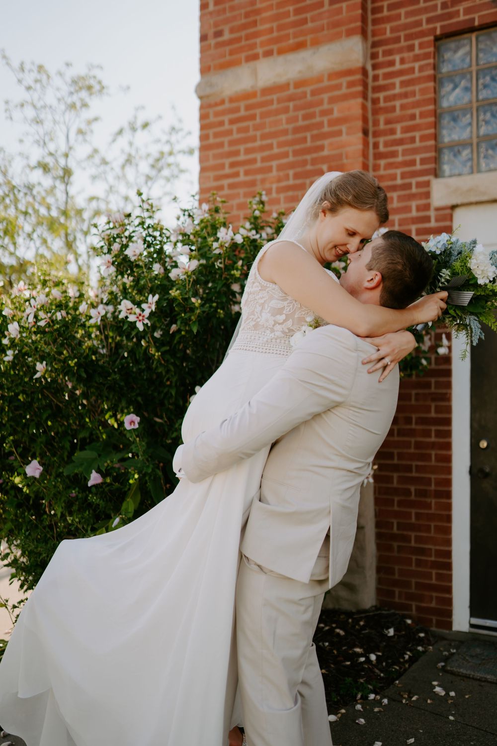 Romantic wedding moment captured against brick wall and garden setting.