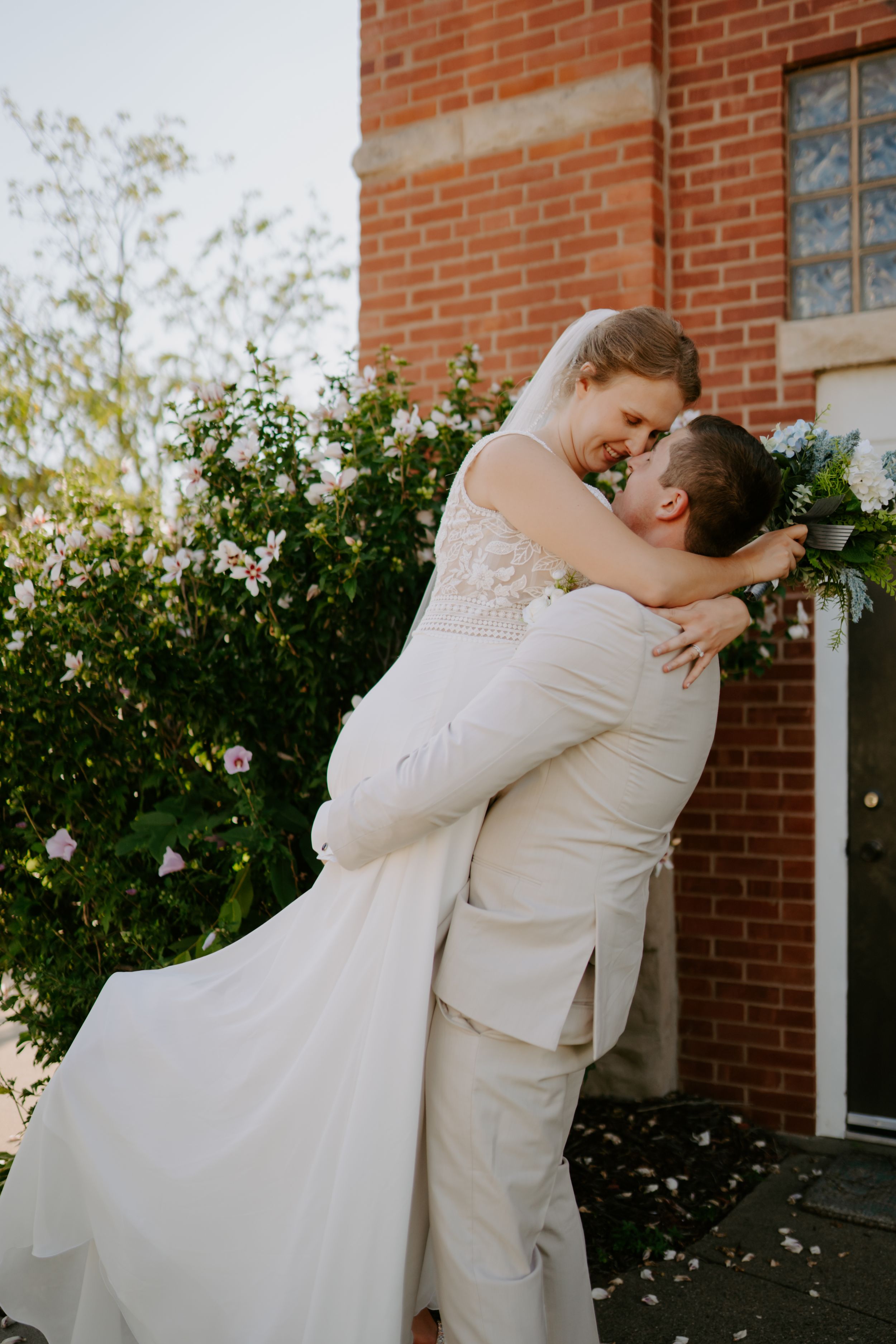 Romantic wedding moment captured against brick wall and garden setting.