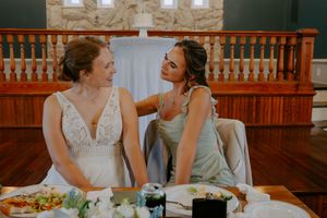 Two wedding guests sharing a joyful moment at a reception table with wooden railing in background.