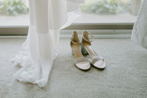 Elegant white and gold bridal shoes displayed on carpet near flowing wedding dress hem.