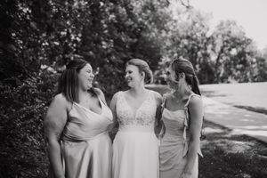 A group in white dresses poses together outdoors in a natural setting for wedding party photos.
