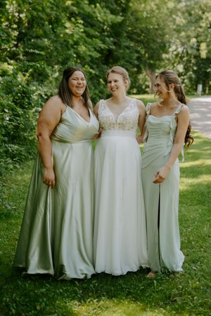 Wedding party members in sage green and white dresses pose together outdoors.