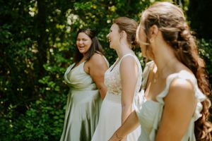 Wedding party members in light colored dresses smile together in a garden setting.