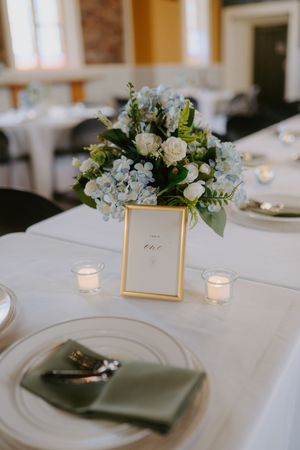 Elegant wedding table setting with blue floral centerpieces and gold frames.