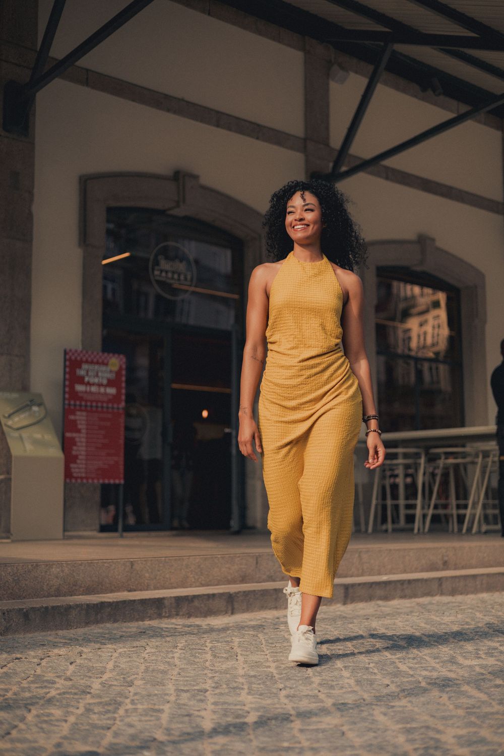 A person in a mustard yellow jumpsuit walks confidently on cobblestone streets.