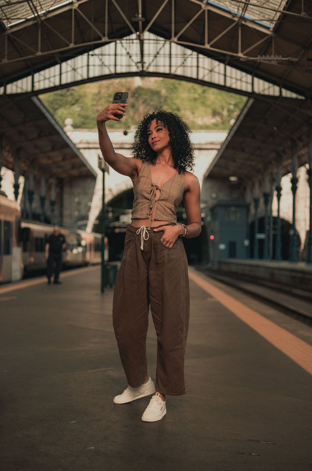 A person takes a selfie at a train station platform under an arched industrial ceiling.