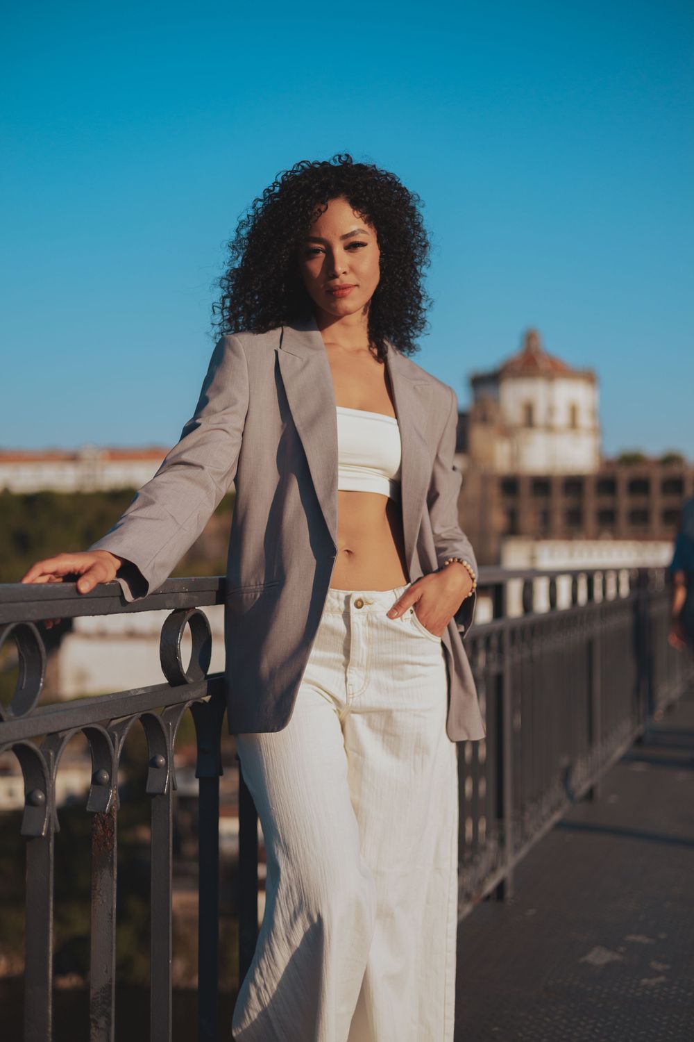 Elegant fashion shoot on bridge with beige blazer and white ensemble against blue sky.