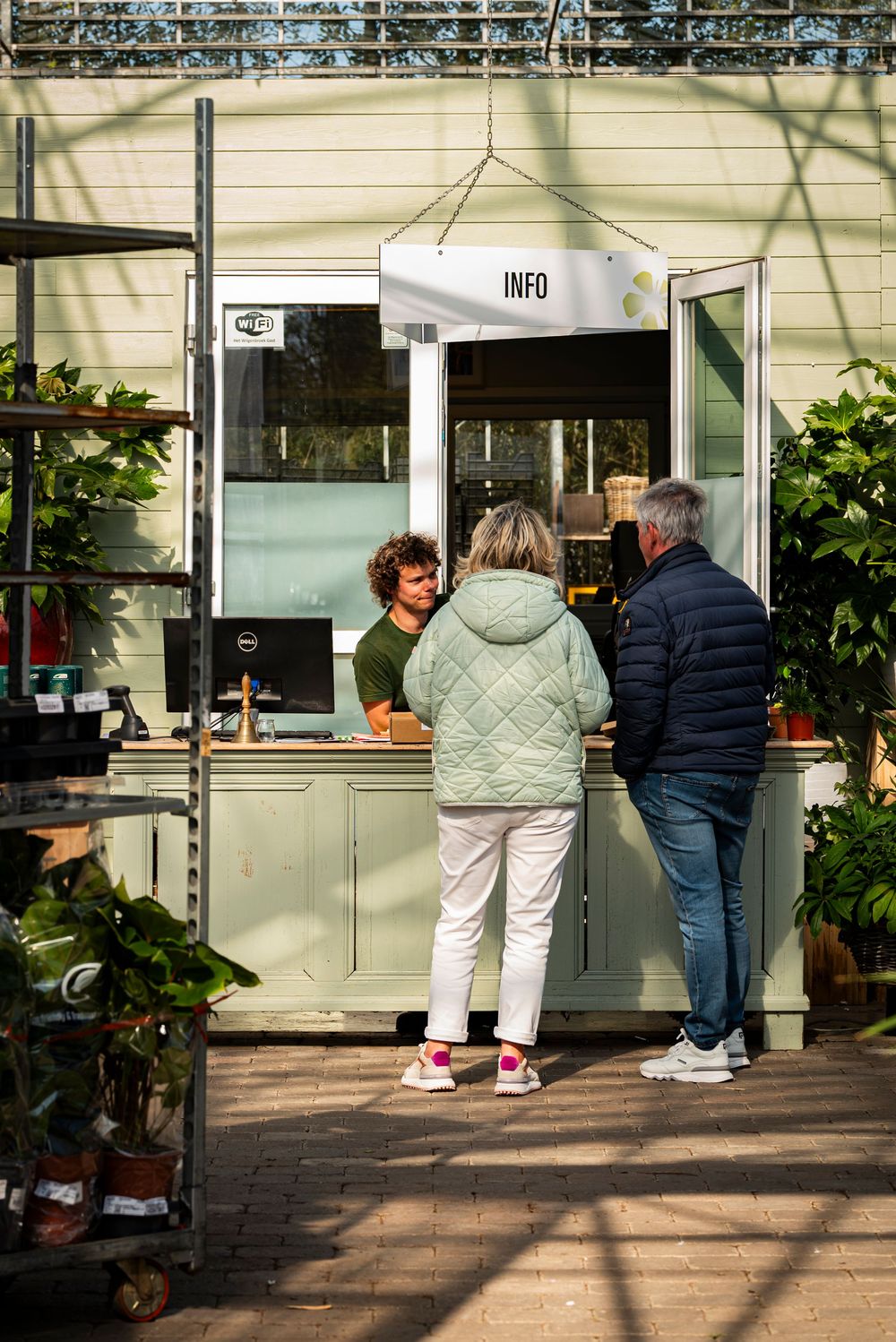 Two customers at an info desk speaking with a staff member inside a garden center.
