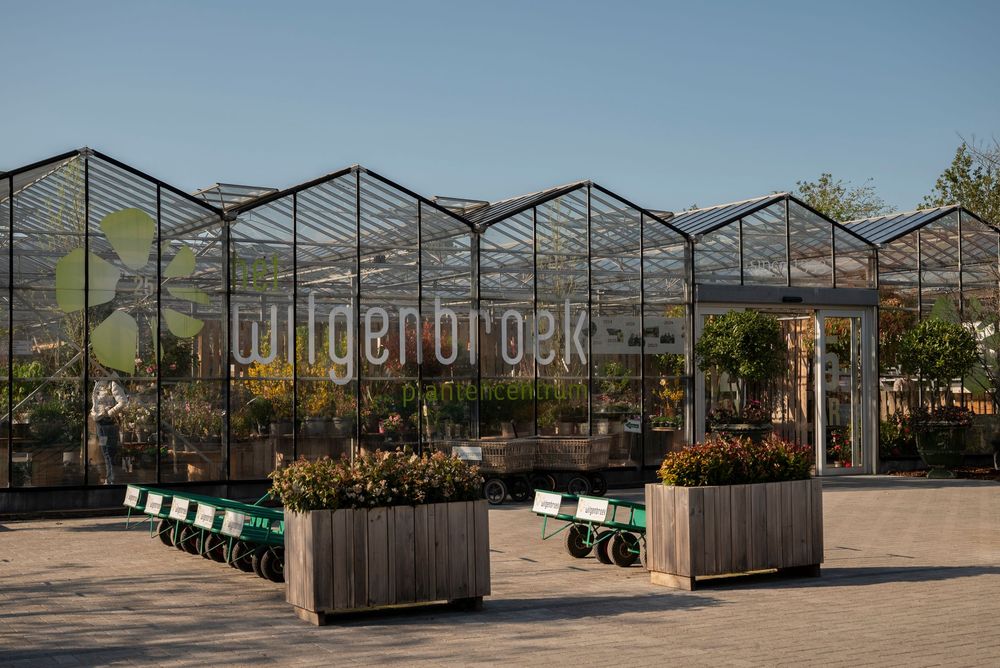 Exterior view of Wilgenbroek garden center greenhouse with shopping carts and outdoor plant displays.