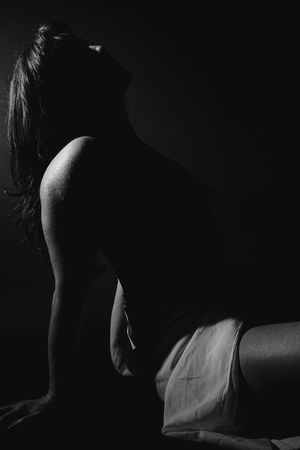 Dramatic black and white artistic boudoir photograph showing silhouette in low light with flowing fabric.