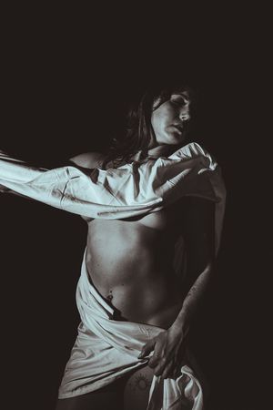 Artistic black and white portrait of a dancer in flowing white fabric against dark background, moving expressively.