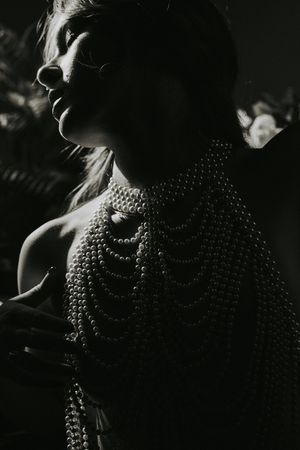 Dramatic black and white portrait showing neck and shoulders adorned with layered metallic chain jewelry in dark lighting.