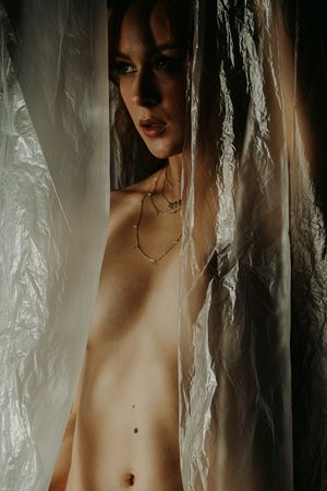 Artistic boudoir portrait with lace curtains creating a soft, ethereal mood.