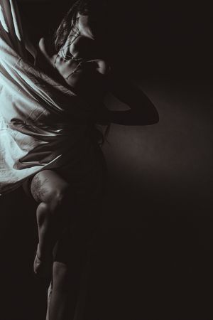Dramatic black and white photo of a dancer in motion with flowing fabric against dark background.