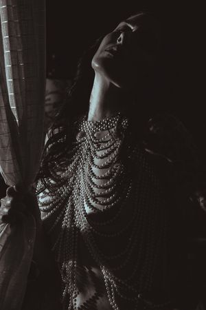 A figure adorned in delicate chain jewelry poses dramatically against dark shadows in monochrome.